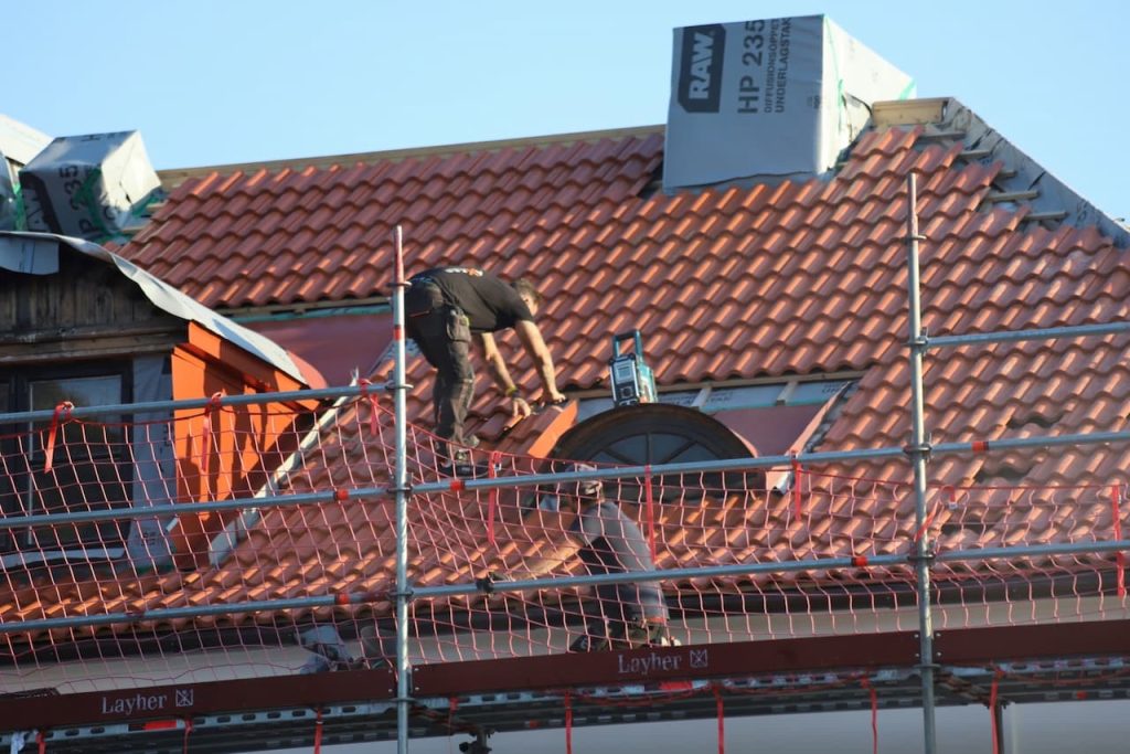 Takläggare lägger nya röda takpannor från en byggnadsställning
