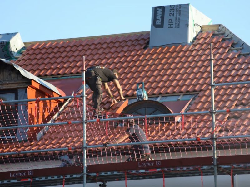 Takläggare lägger nya röda takpannor från en byggnadsställning