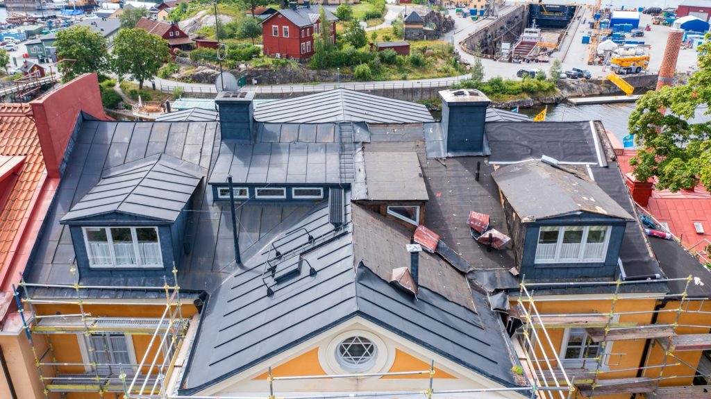 Gammal takplåt rivs och underlagspapp friläggs på ett stadshus